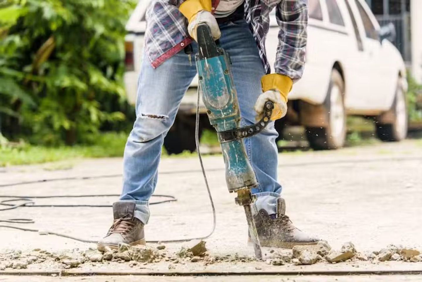 a person wearing safety equipment while breaking concrete slab with heavy-duty breaker