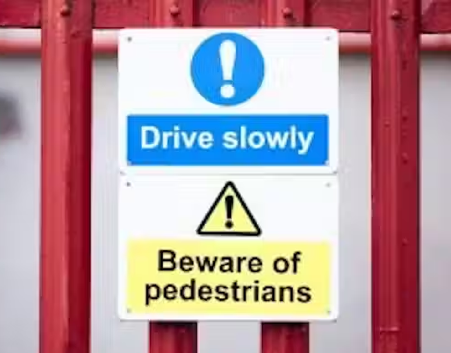 Two warning signs attached to a metal fence: Drive slowly and beware of pedestrians