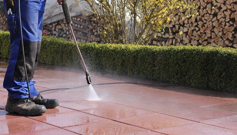 person in a safety shoes cleaning pavement with a pressure washer