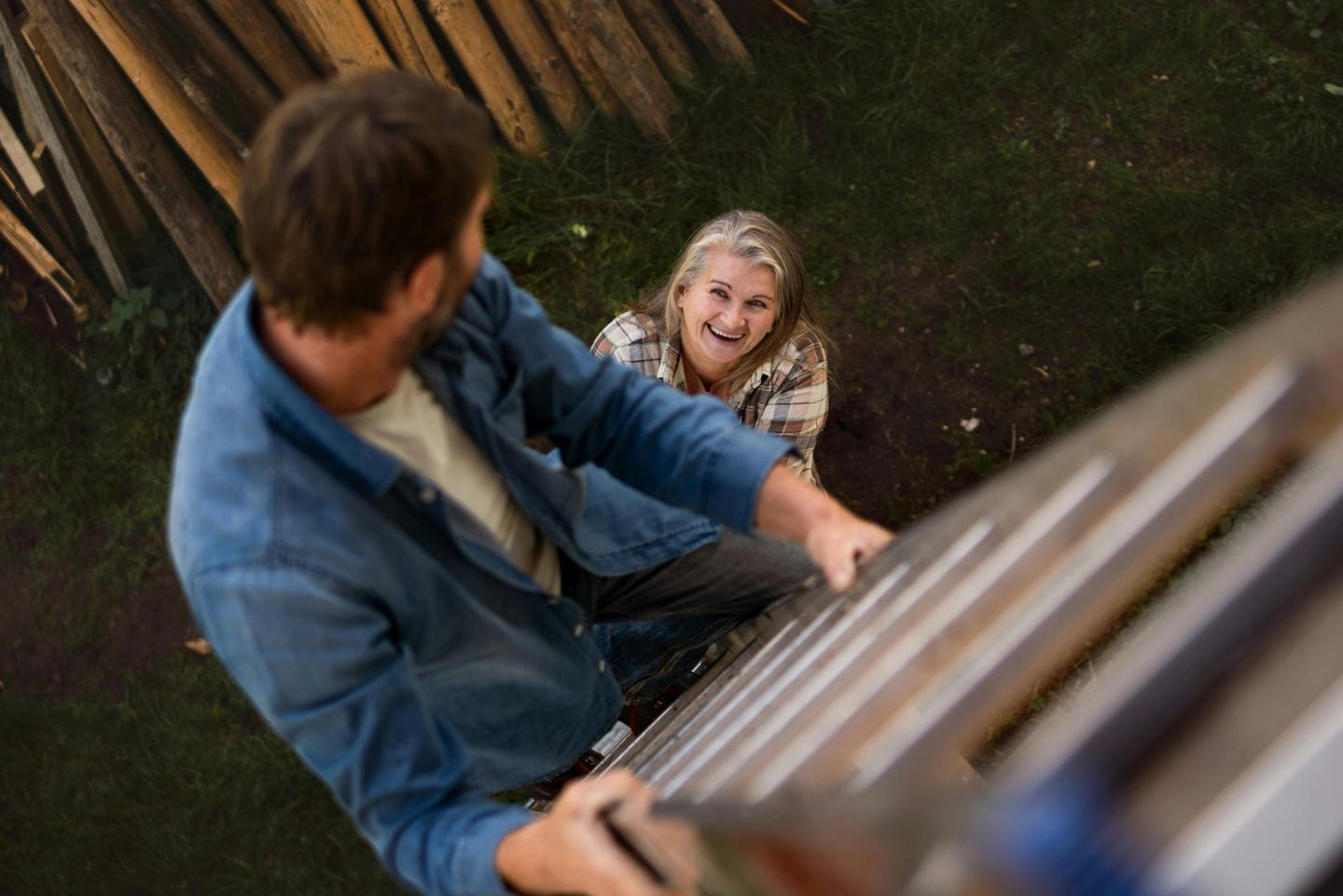 Man climbing a ladder being held by a woman