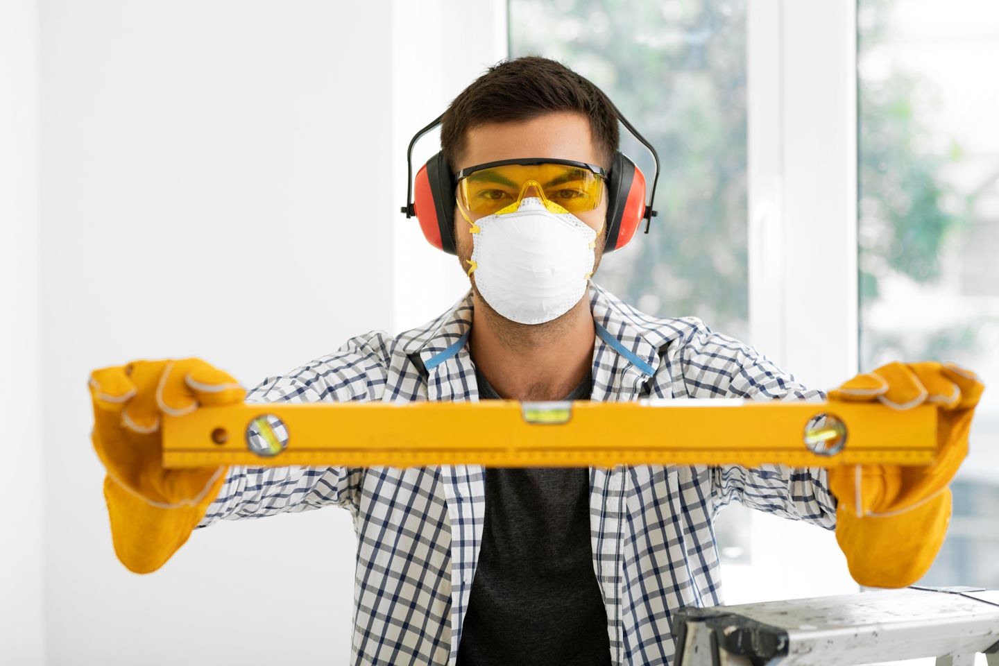 Man holding spirit level with safety protection equipment including safety glasses a dust mask and ear defenders