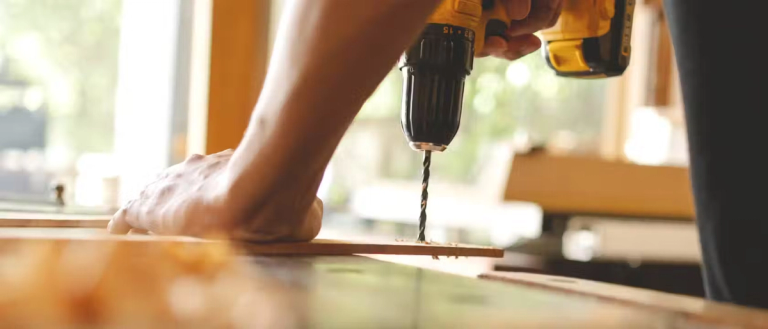 A DIYer using a drill on a piece of wood.