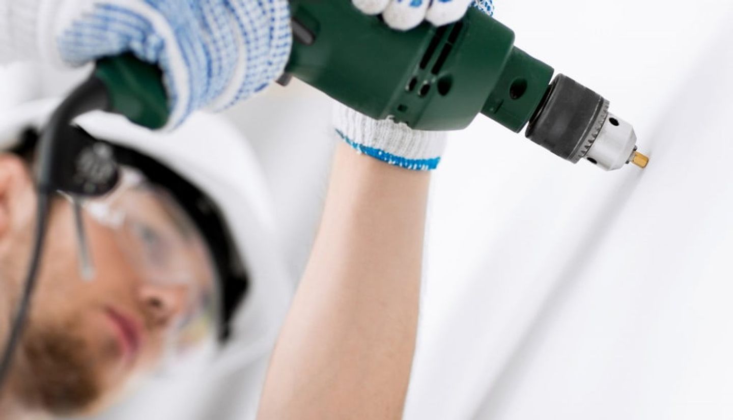 man in safety glasses and helmet drilling into the wall