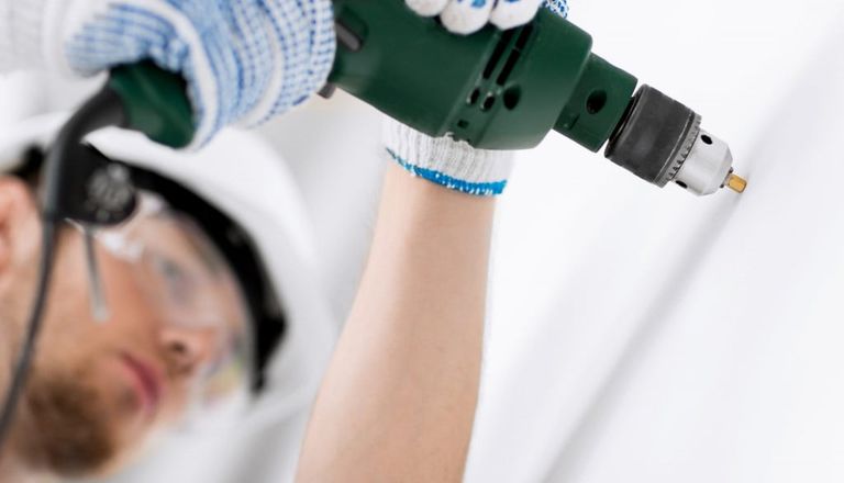 man in safety glasses and helmet drilling into the wall