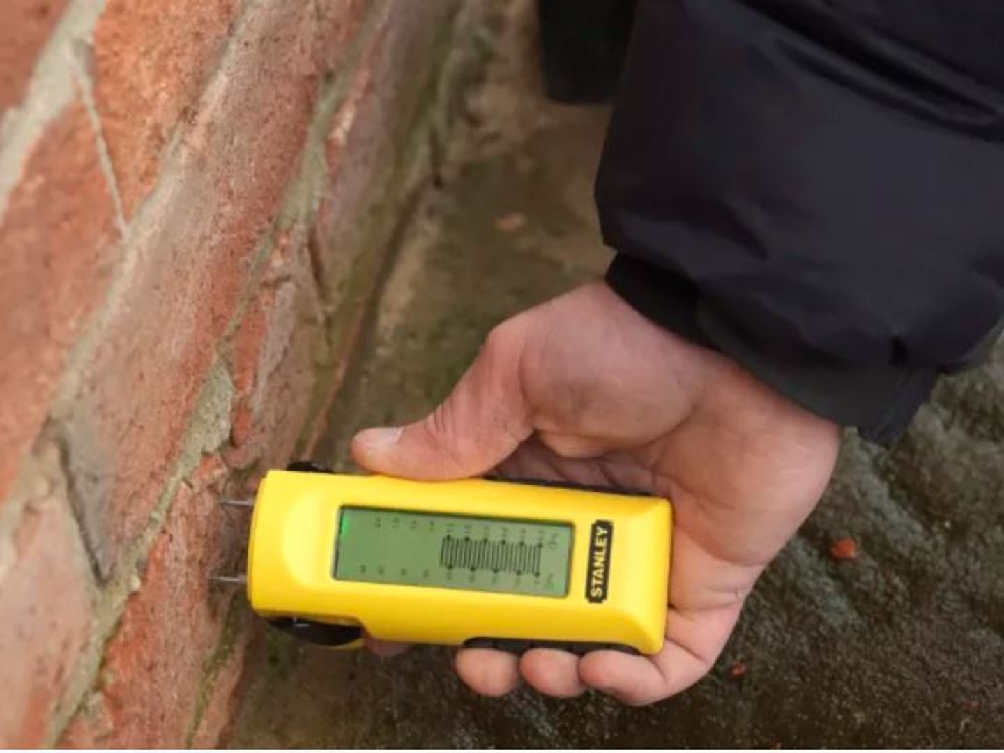 person using yellow stanley moisture meter to measure moisture in brick wall