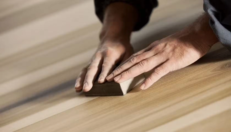 Someone sanding a floor with a sanding block.