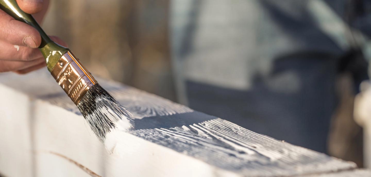 Someone painting the garden fence with a paint brush.