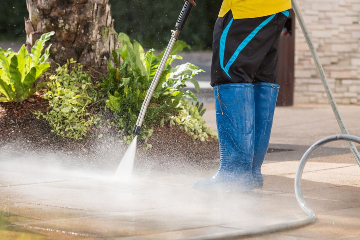 A person wearing wellies cleaning pavement using pressure washer