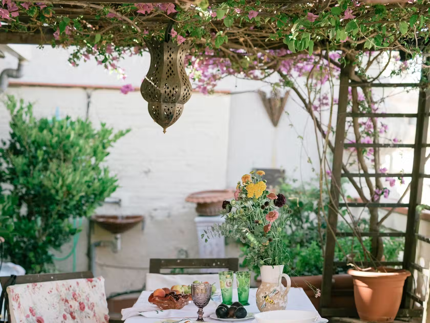 A garden table with fruit, glasses and flowers.