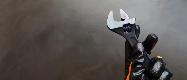 A person wearing work gloves, holding a wrench.