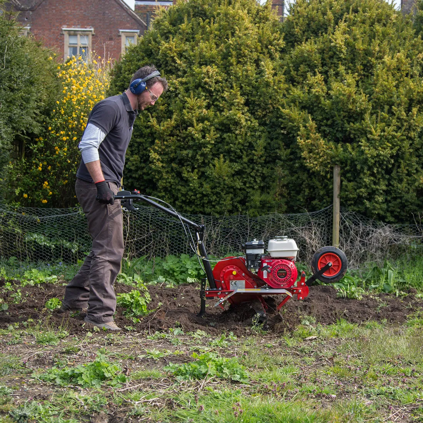 Man wearing PPE rotavating soil.