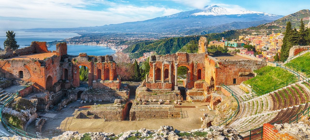 Ruins of ancient Greek theater in Taormina and Etna volcano in the background. Coast of Giardini-Naxos bay, Sicily, Italy, Europe.