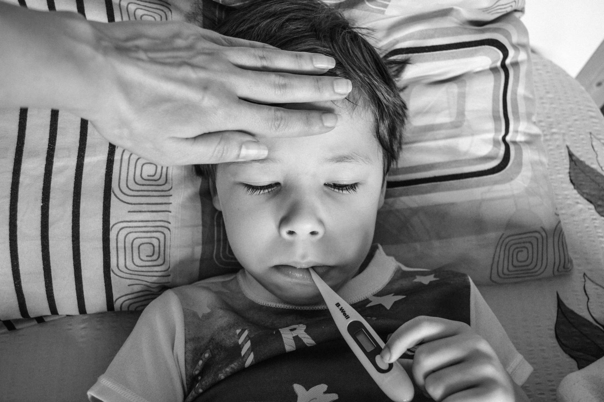 Un enfant se reposant avec un thermomètre, surveillé par une main bienveillante, à l'intérieur