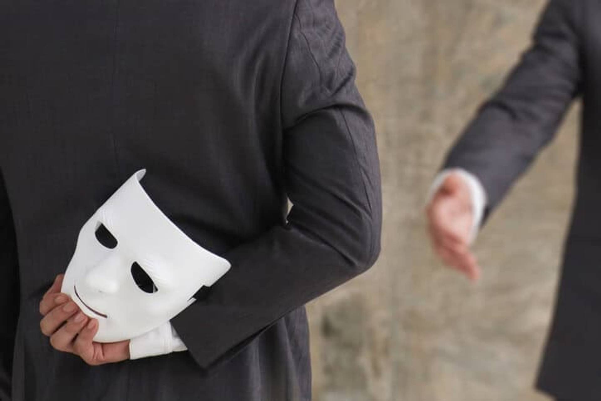 Personne tenant un masque blanc derrière son dos.