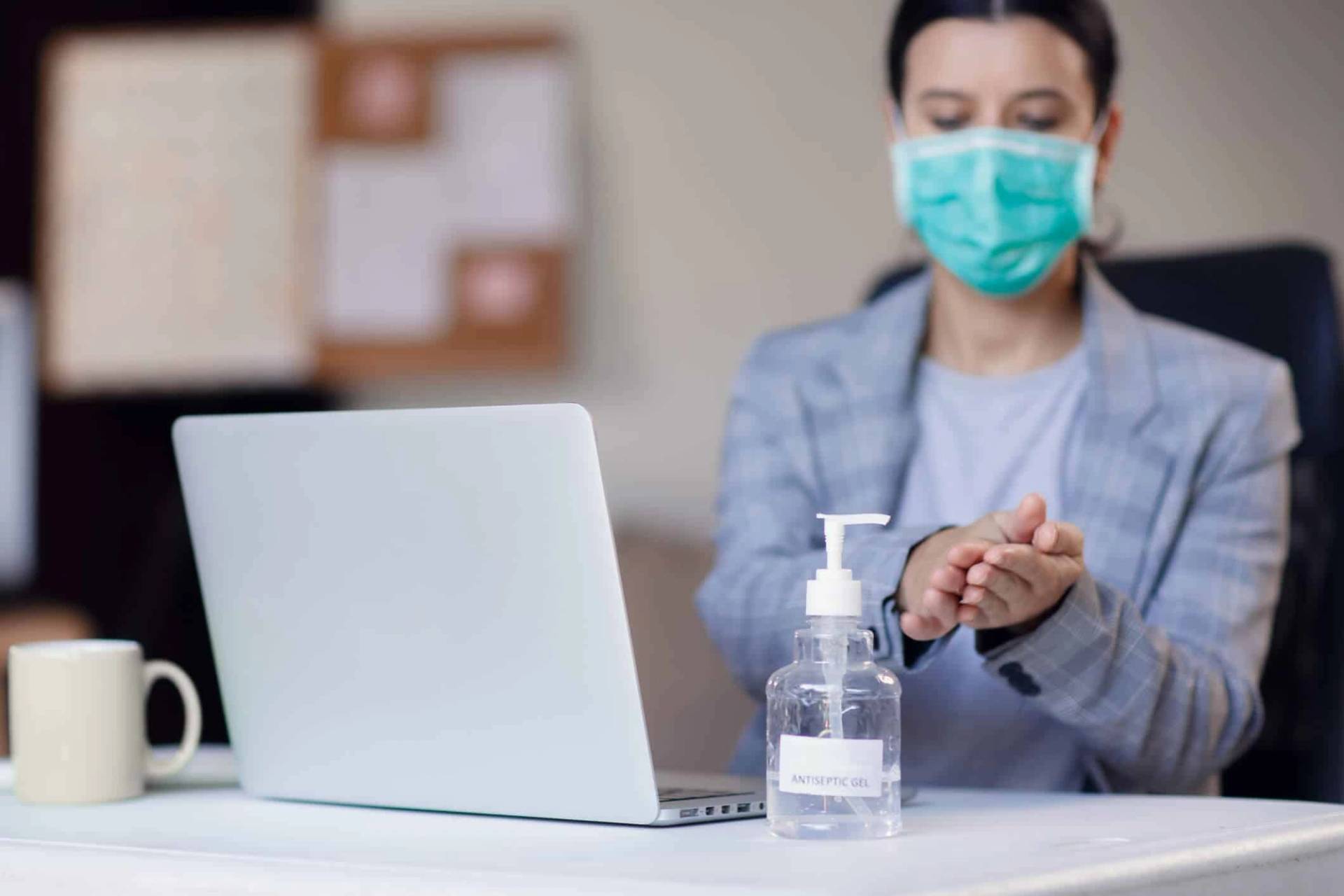 Adulte masqué devant un ordinateur avec du gel hydroalcoolique.