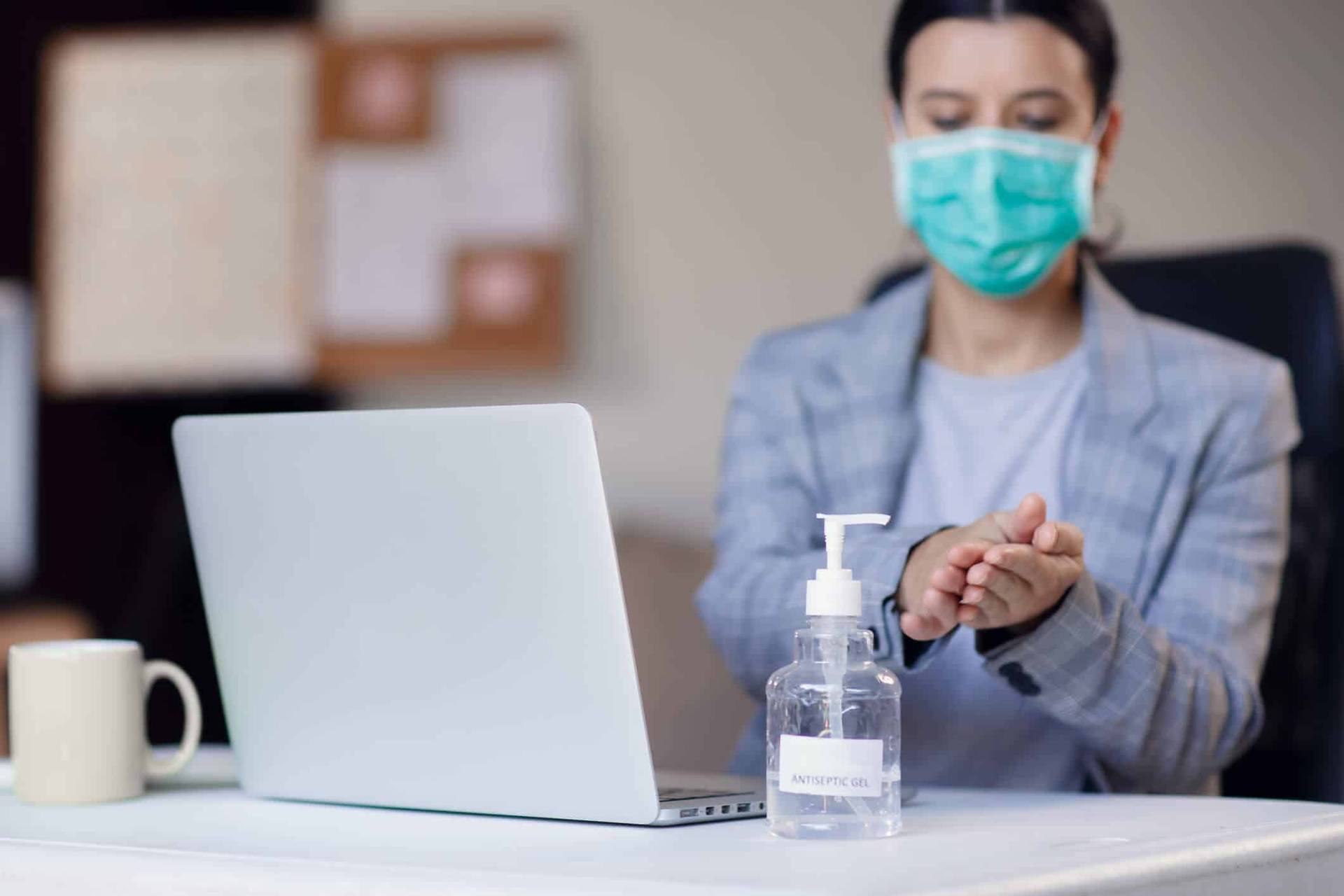 Adulte masqué devant un ordinateur avec du gel hydroalcoolique.