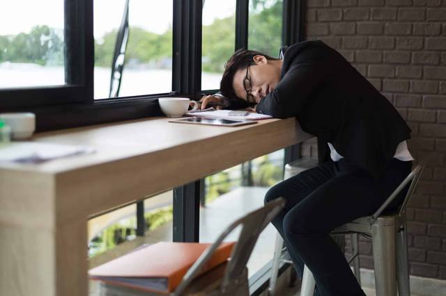 Personne endormie, tête posée sur une table près d’une fenêtre.