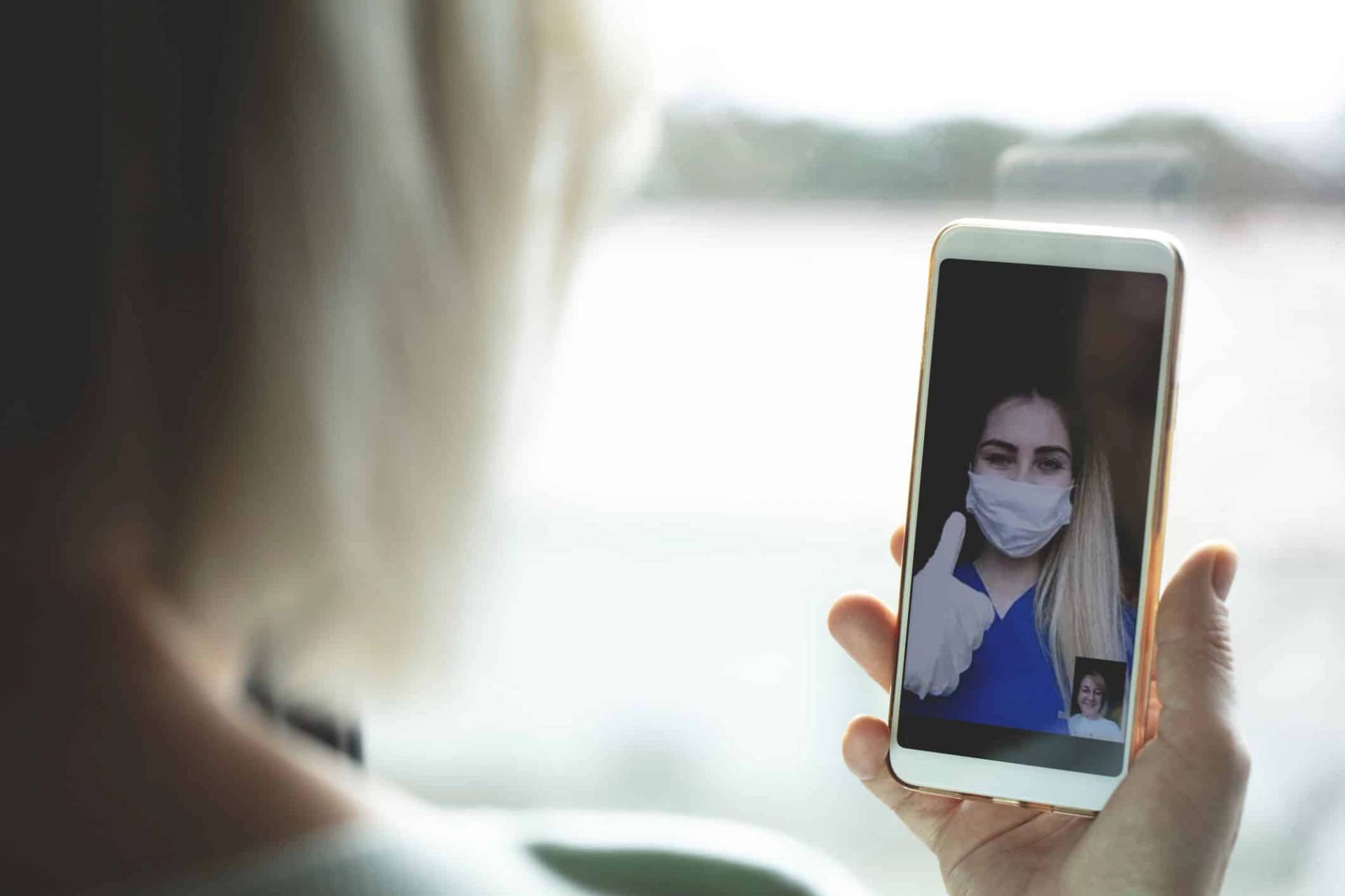 Personne utilisant son téléphone pour un appel vidéo avec une personne masquée.