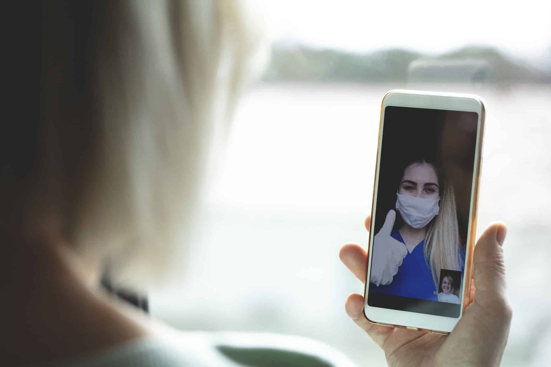 Personne utilisant son téléphone pour un appel vidéo avec une personne masquée.