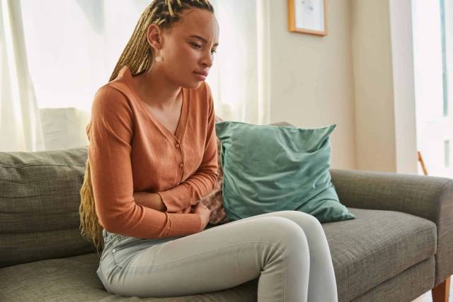 Femme assise sur un canapé, une main sur le bas du ventre.