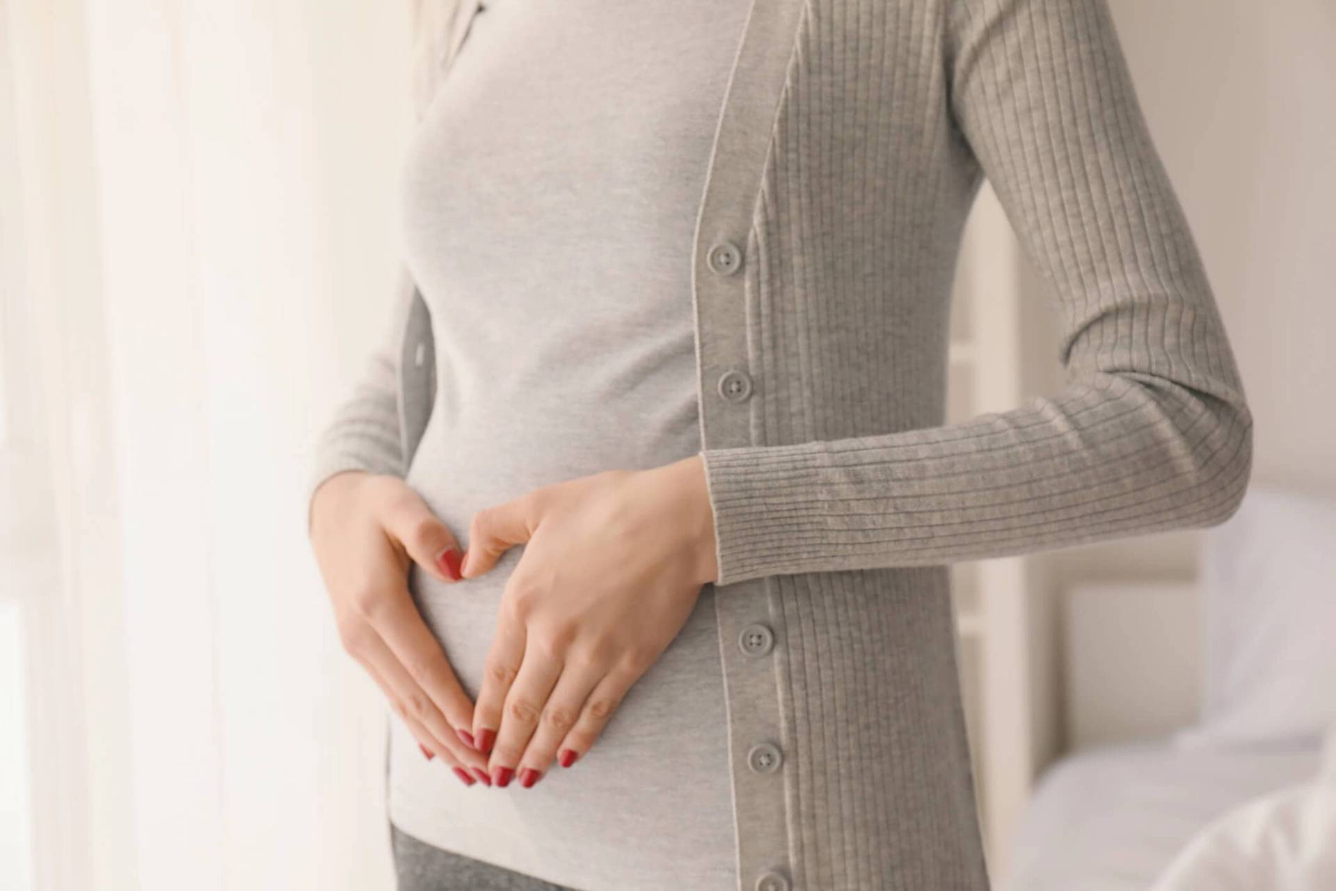 Femme enceinte qui se touche le ventre en faisant un coeur avec ses mains