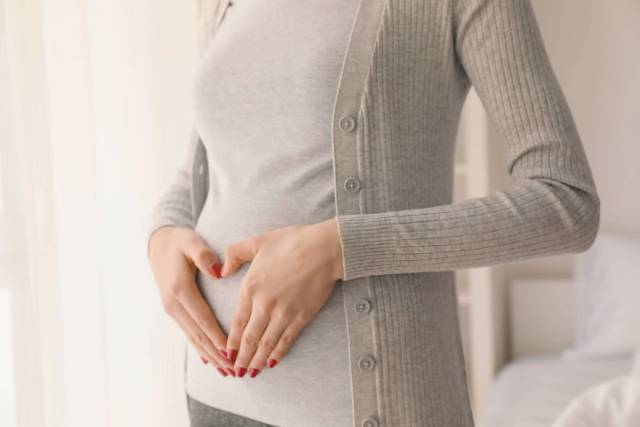 Femme enceinte qui se touche le ventre en faisant un coeur avec ses mains