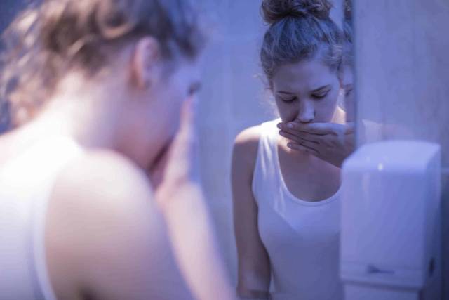 Personne penchée au-dessus d’un lavabo, la main devant la bouche.
