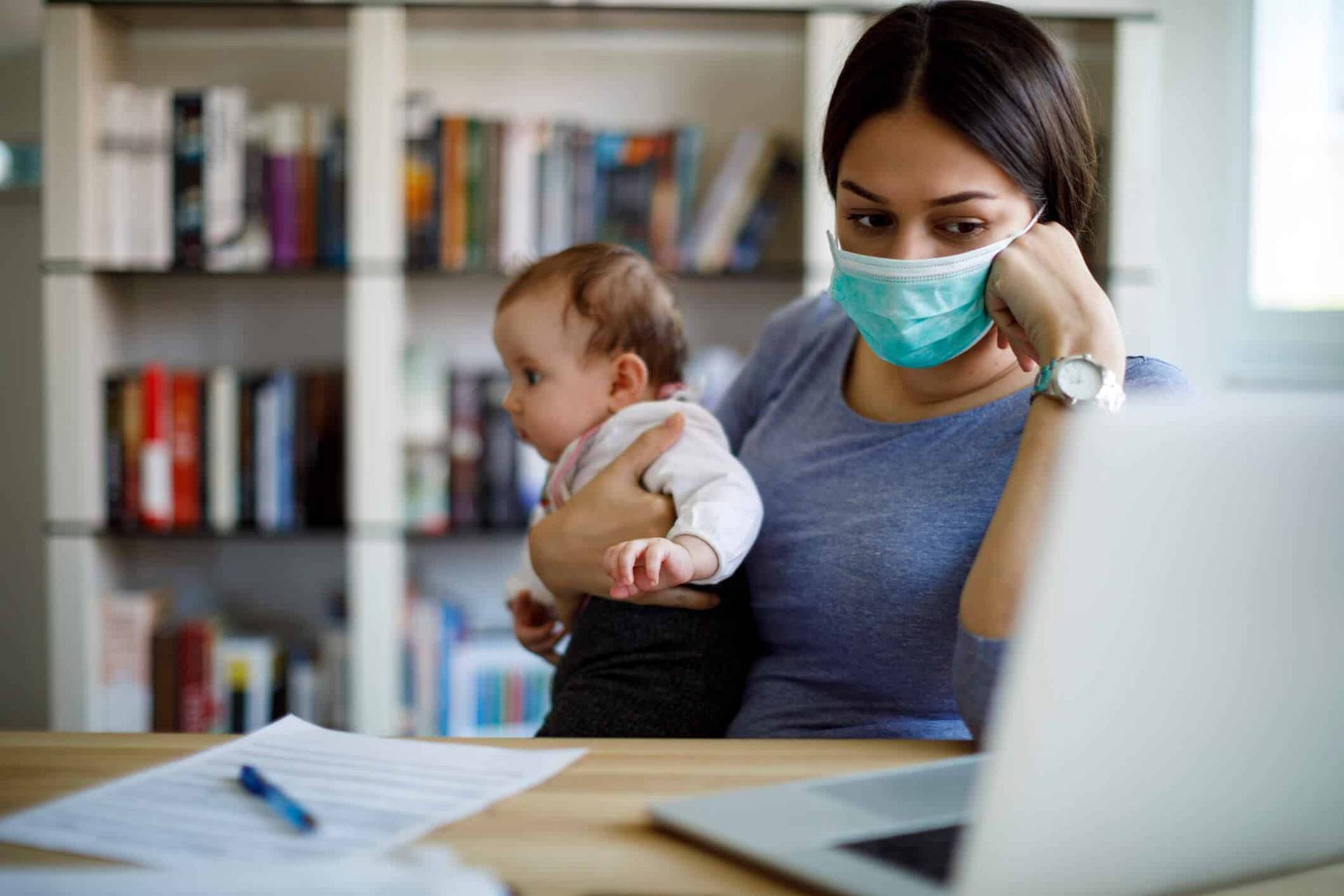 Adulte masqué portant un bébé devant un ordinateur.