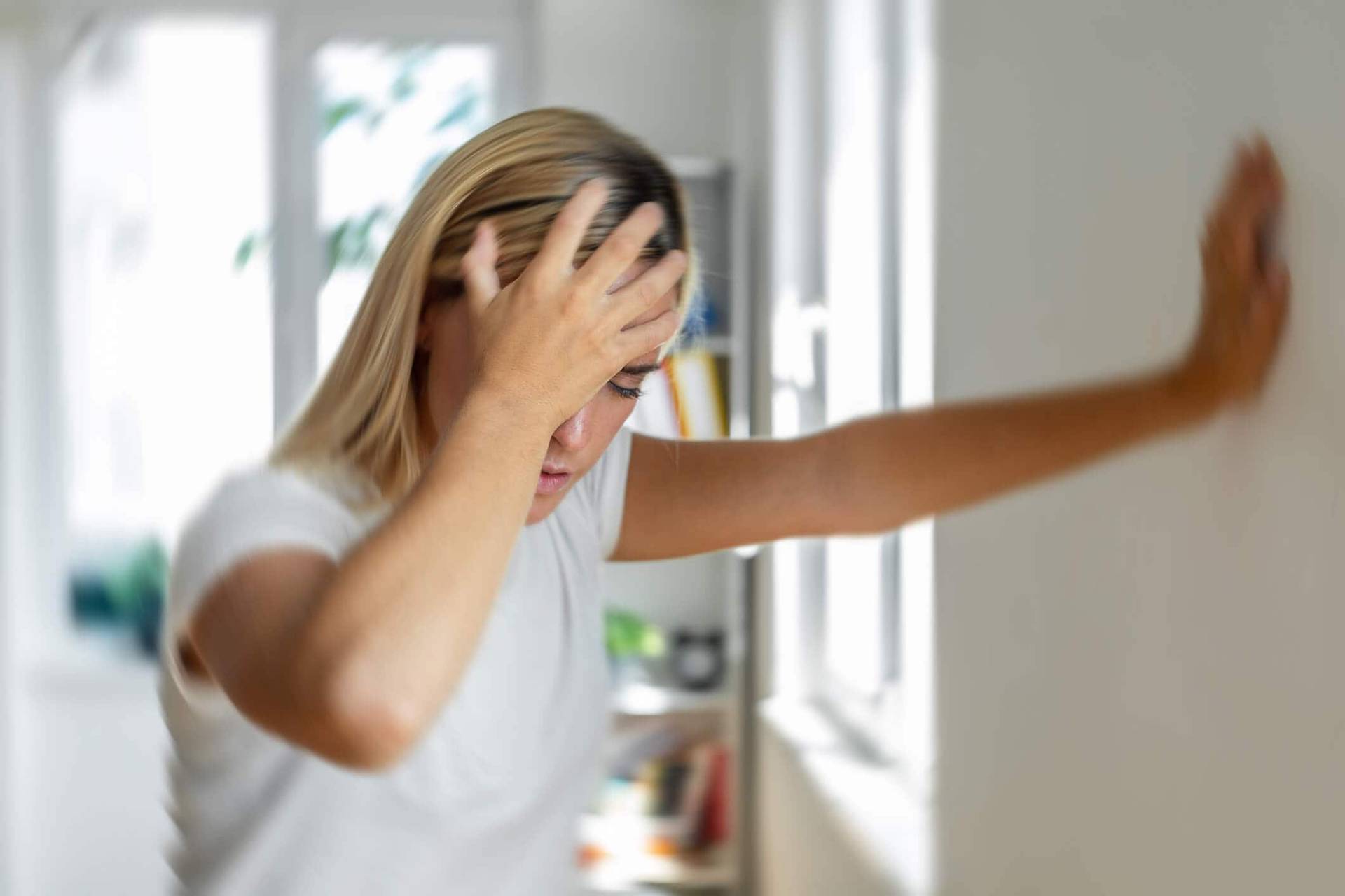 Femme portant une main à son front et prenant appui sur un mur.