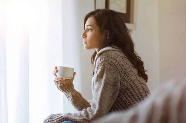 Femme assise près d’une fenêtre avec une tasse.