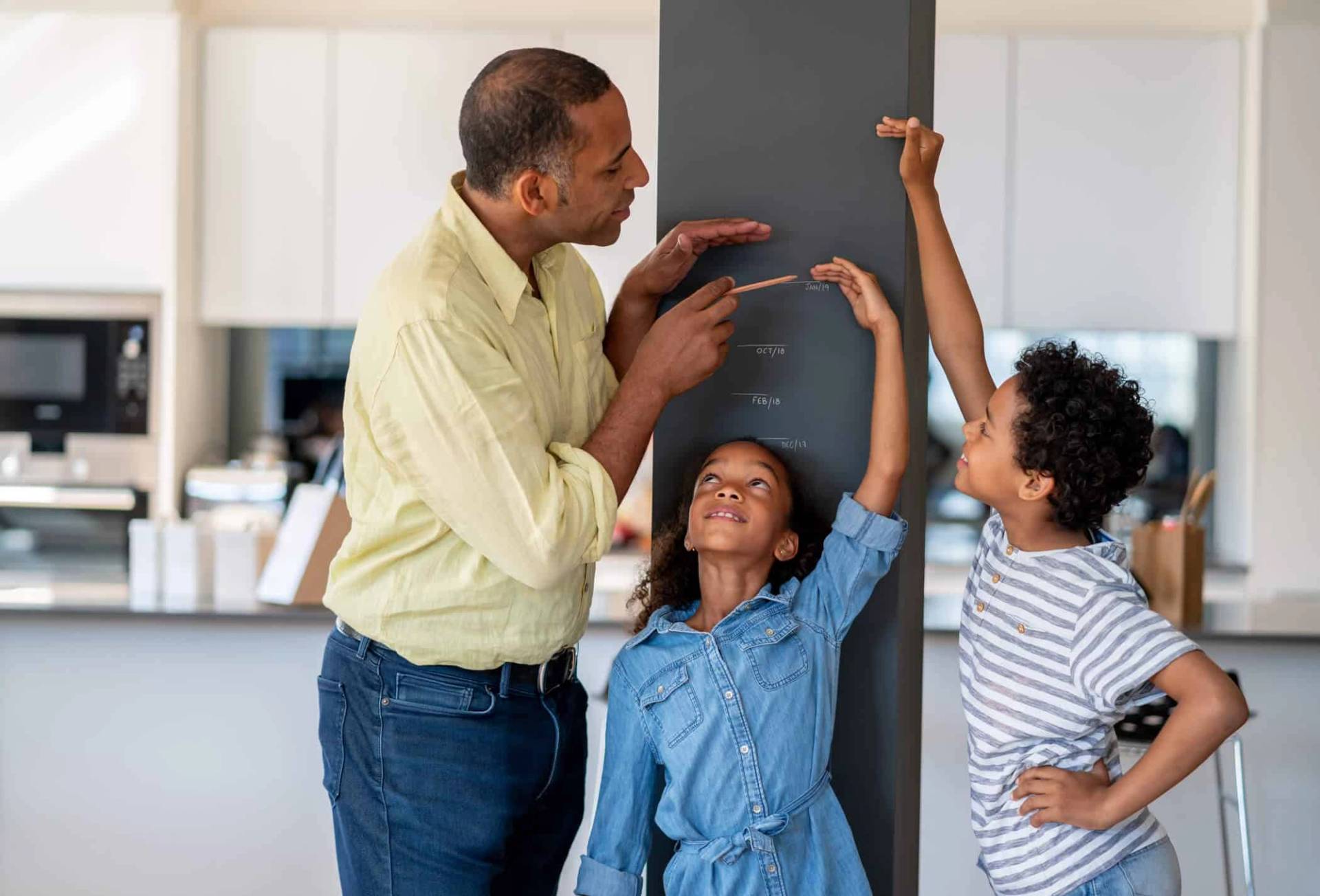 Adulte mesurant la taille de deux enfants contre un mur.