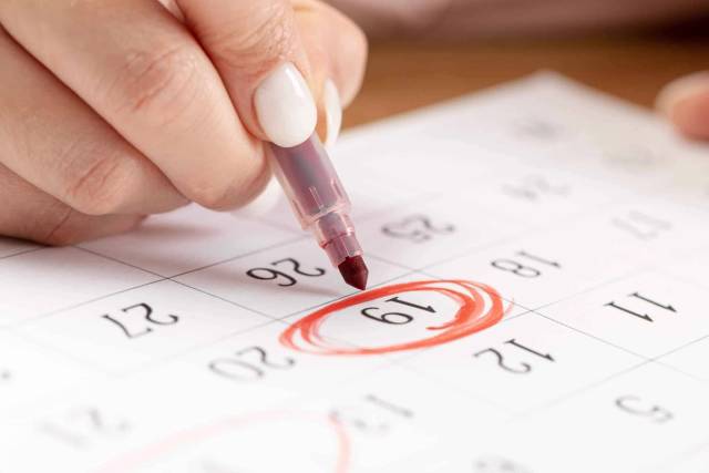 Main entourant une date sur un calendrier.