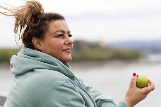 Femme en vêtement de sport tenant une pomme à l’extérieur.