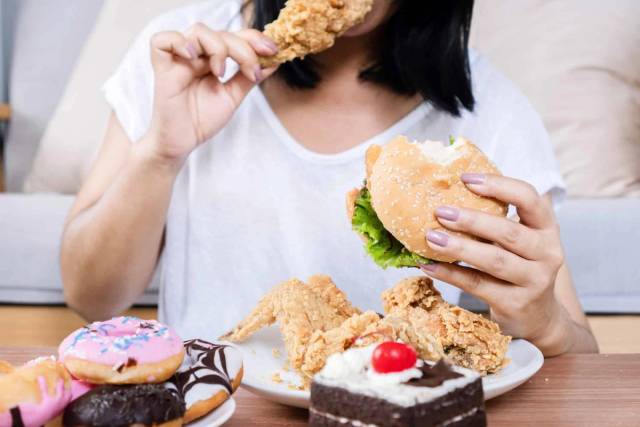 Personne devant un plateau de burgers, frites, poulet et pâtisseries.