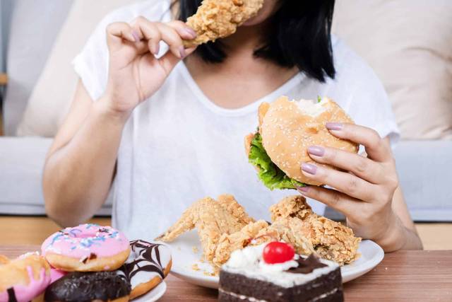 Personne devant un plateau de burgers, frites, poulet et pâtisseries.