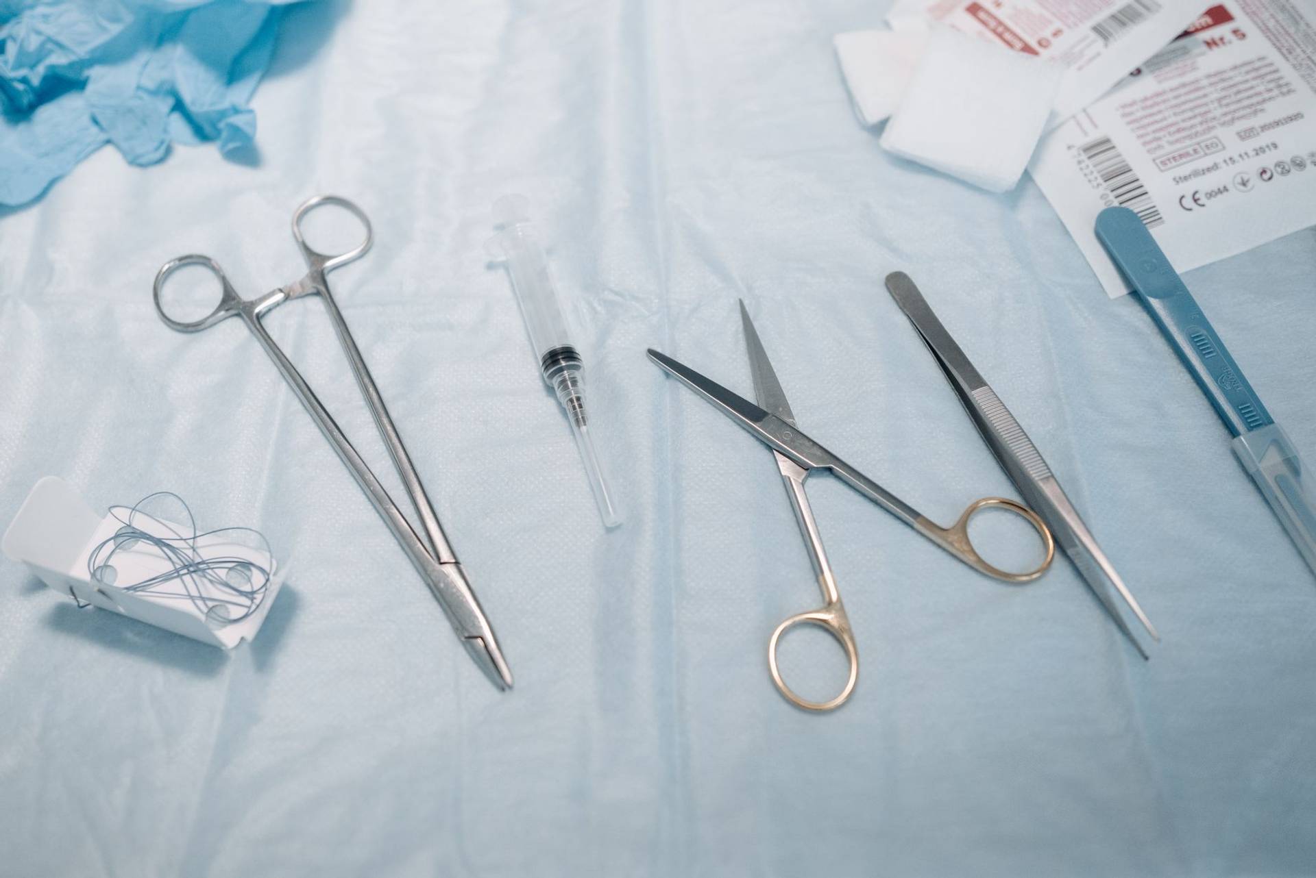 Instruments médicaux, seringue et compresses disposés sur un champ bleu.