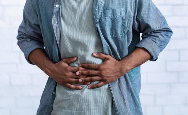 Homme debout avec les mains sur l’abdomen.