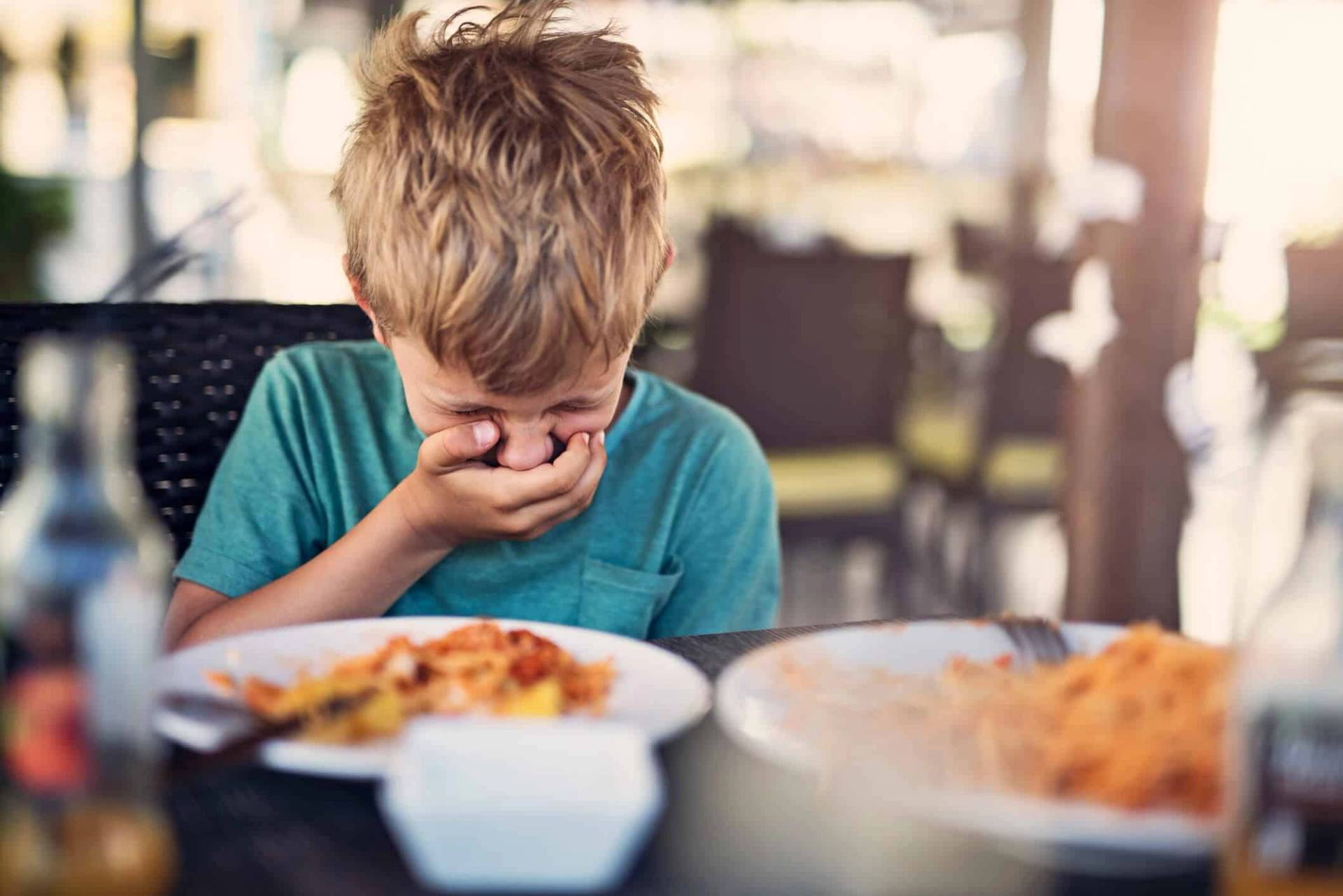 Enfant devant une assiette, la main sur la bouche.