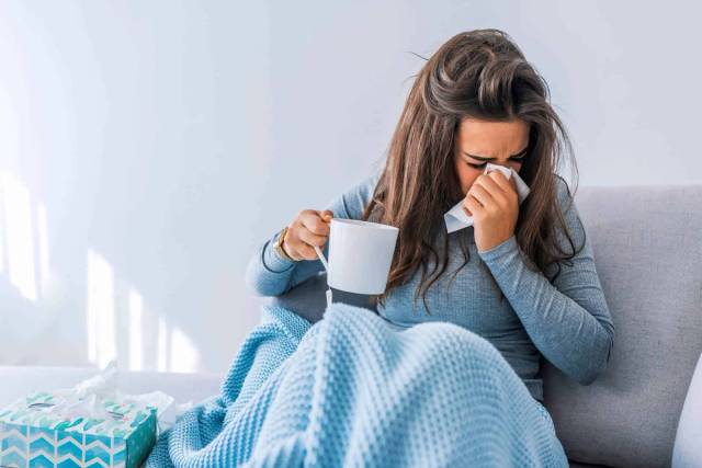 Femme sur un canapé, une tasse et un mouchoir à la main.