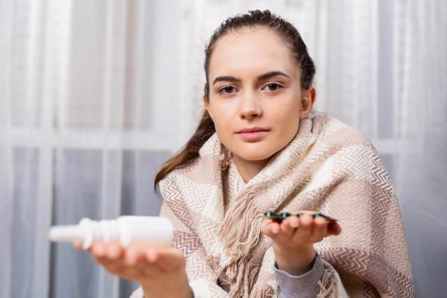 Femme enveloppée dans une couverture tenant des médicaments.