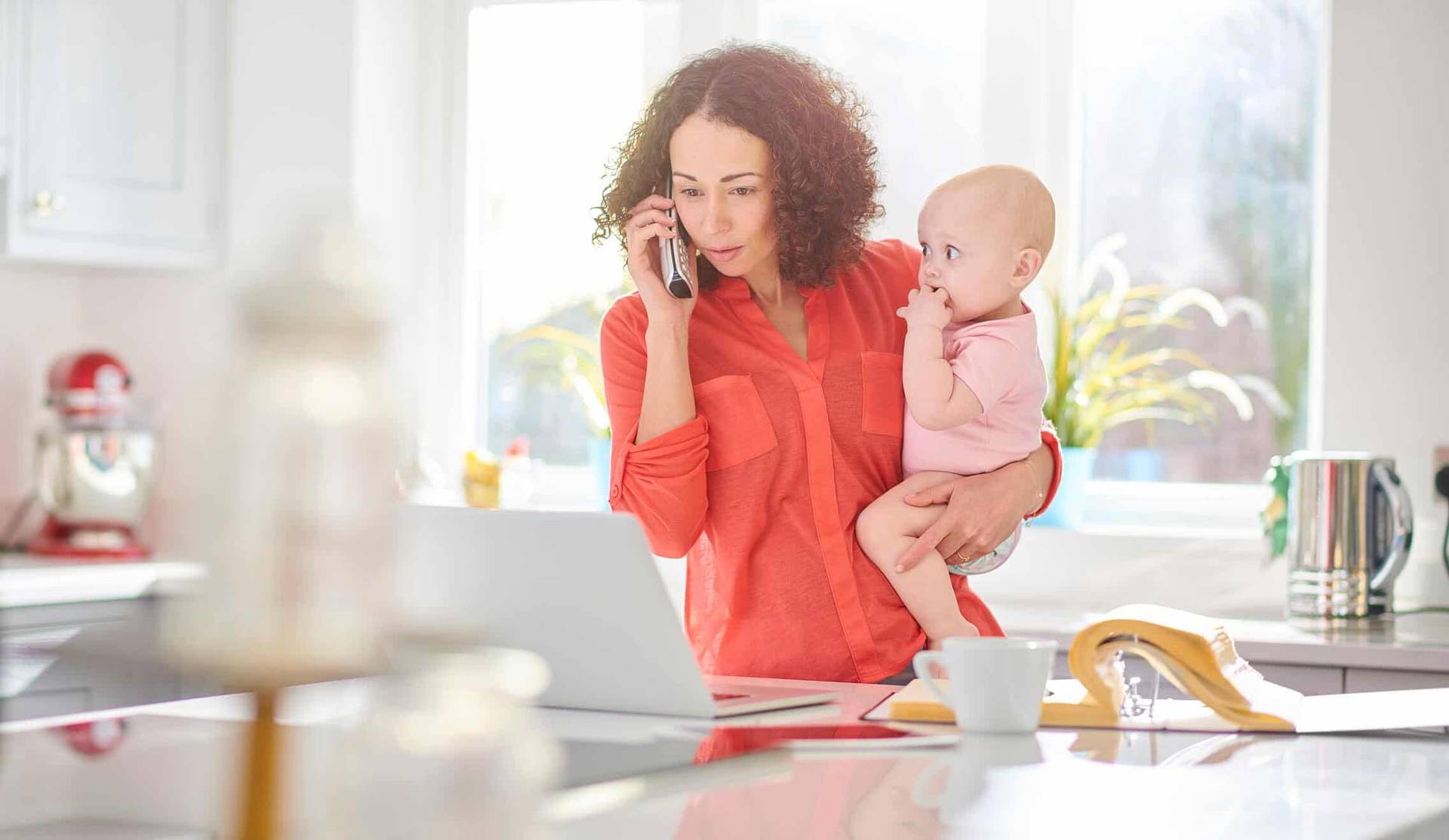 Adulte téléphonant dans une cuisine en portant un bébé.