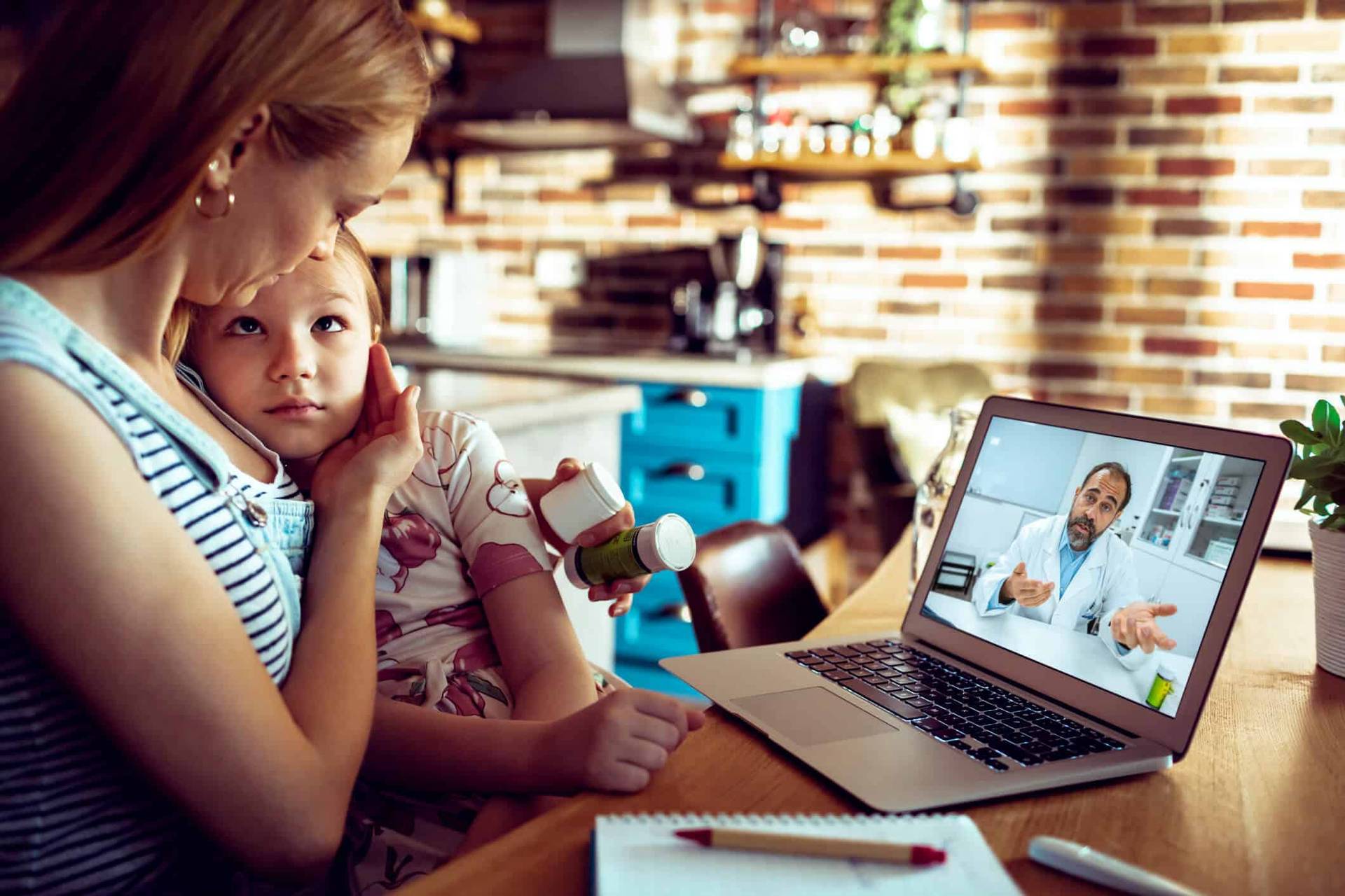 Adulte et enfant devant un ordinateur affichant un médecin en appel vidéo.