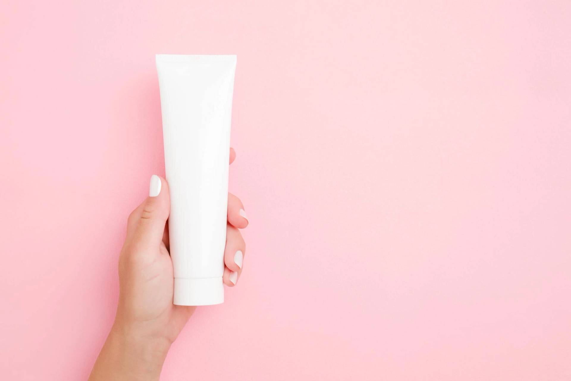 Main tenant un tube blanc sur fond rose.