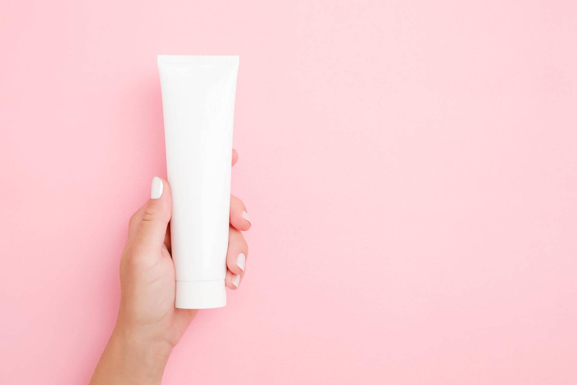 Main tenant un tube blanc sur fond rose.