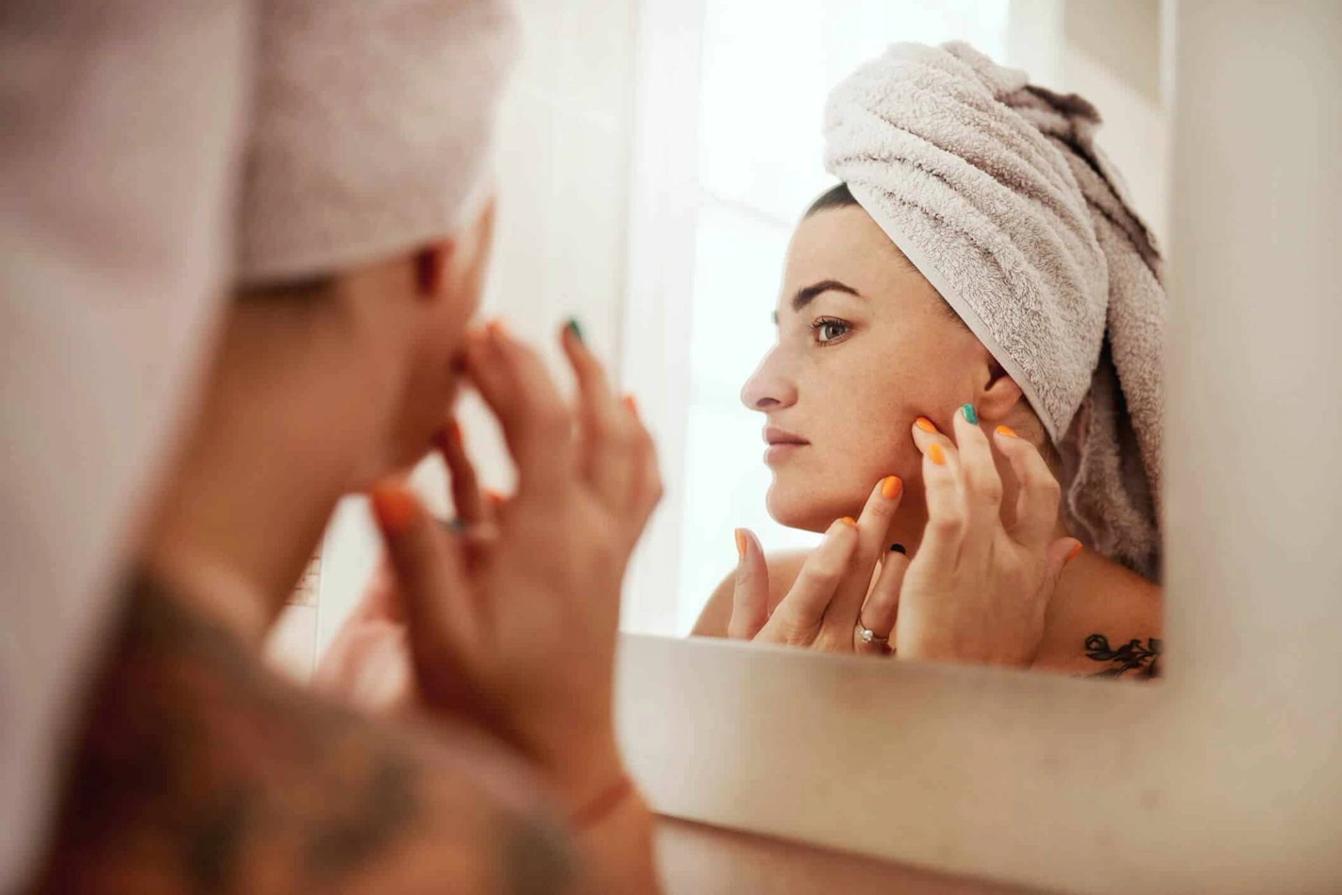 Personne observant sa peau dans un miroir.