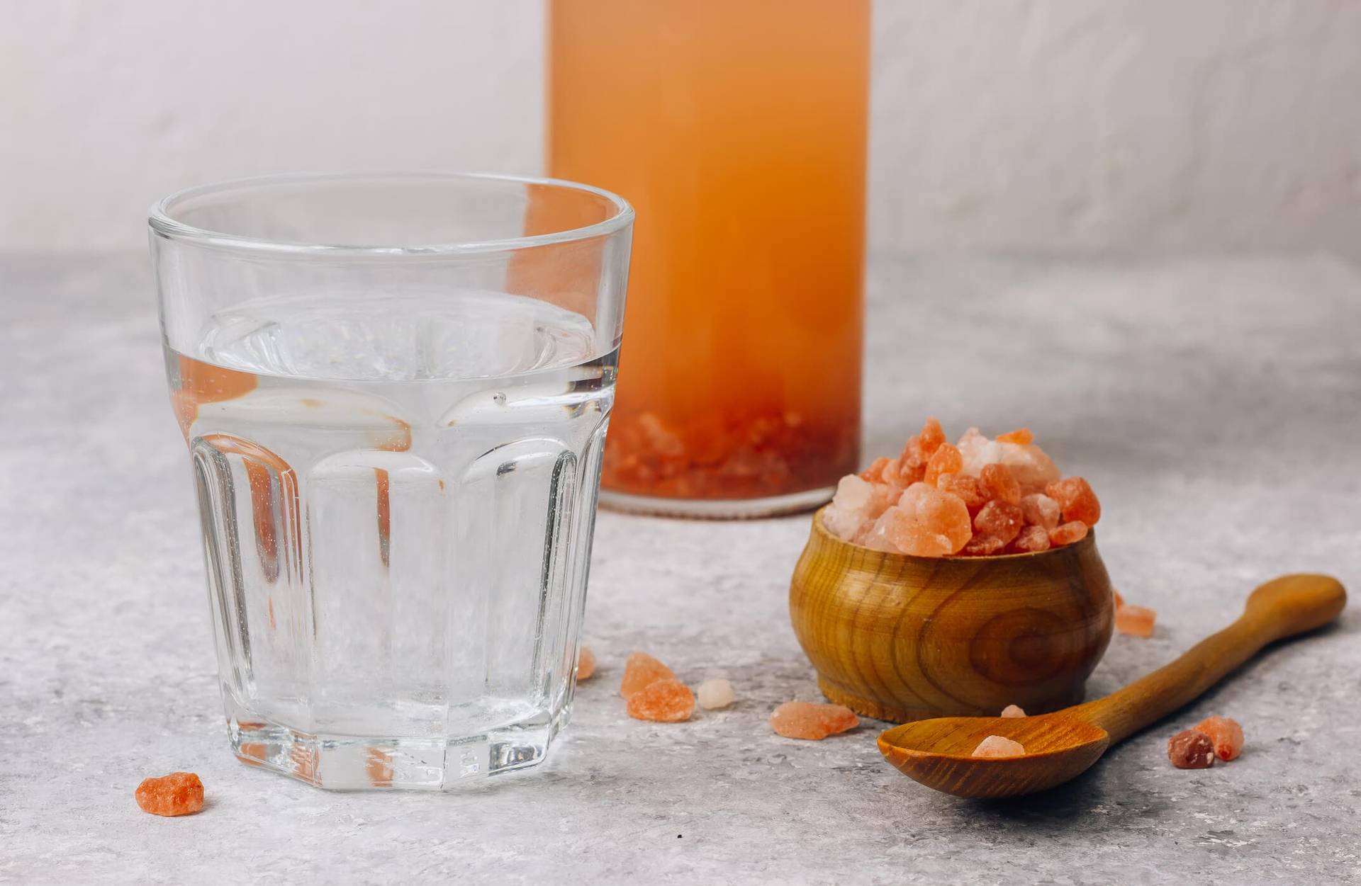 Verre d’eau, récipients et petits cristaux orangés sur une table.