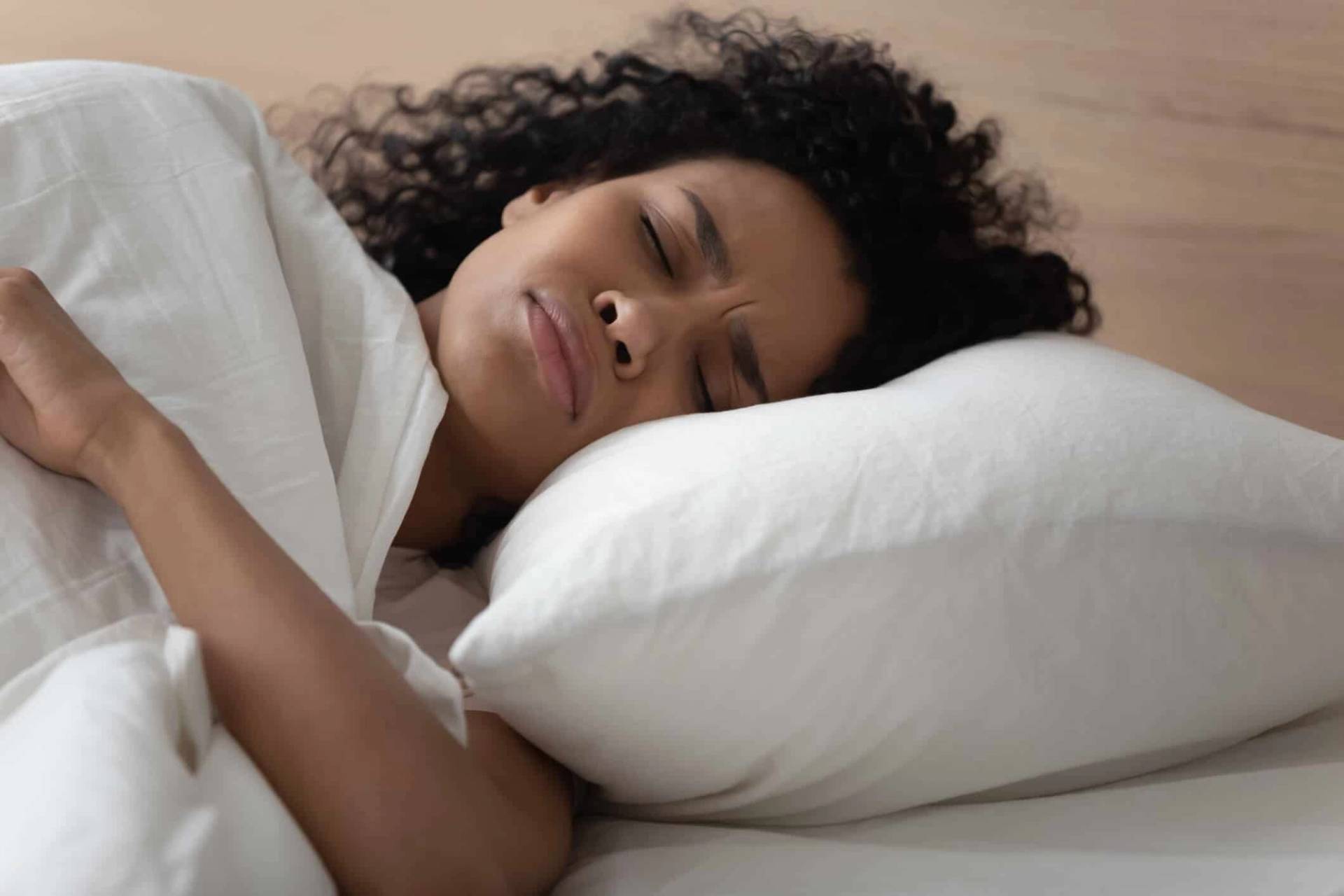 Femme allongée dans un lit, une main posée sur le ventre.