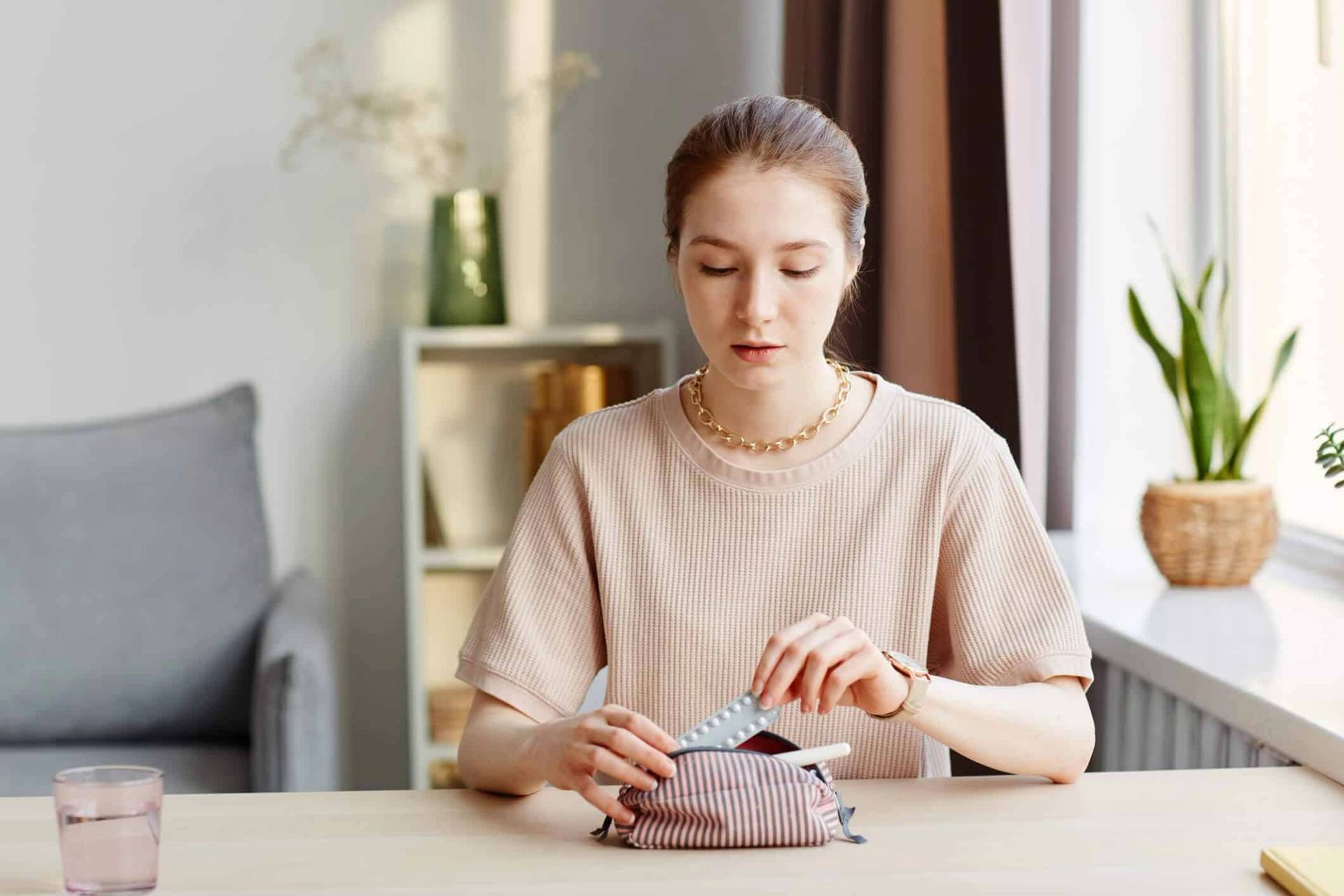Femme assise à une table, regardant un emballage de médicaments.