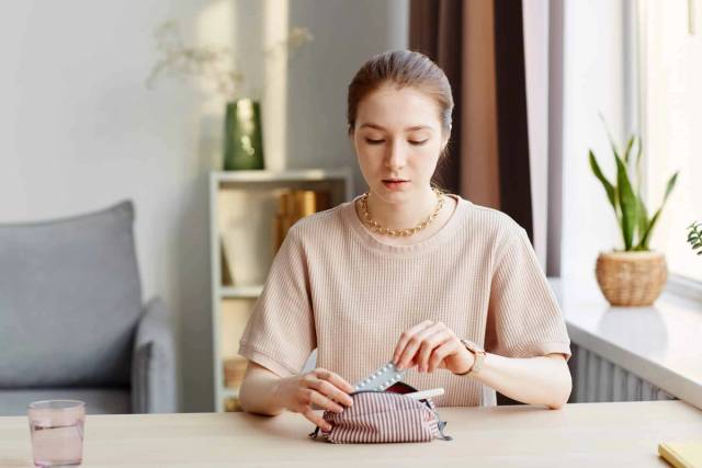 Femme assise à une table, regardant un emballage de médicaments.