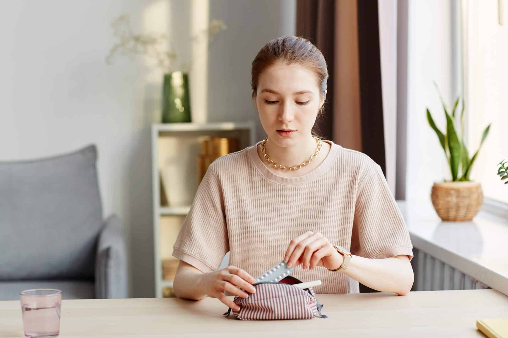 Femme assise à une table, regardant un emballage de médicaments.